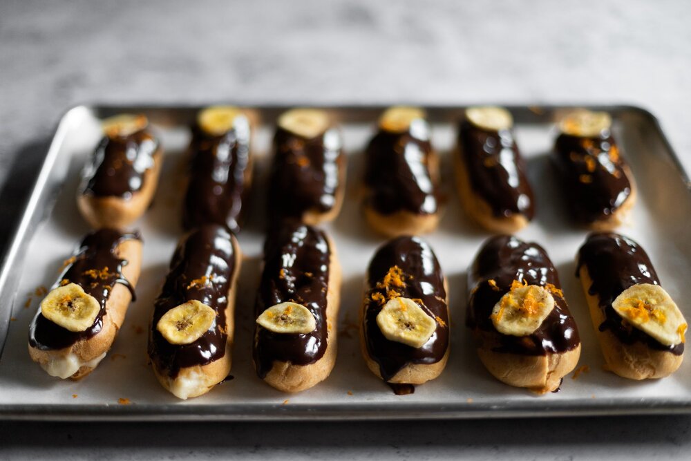 eclairs topped with chocolate ganache, a banana slice, and orange zest
