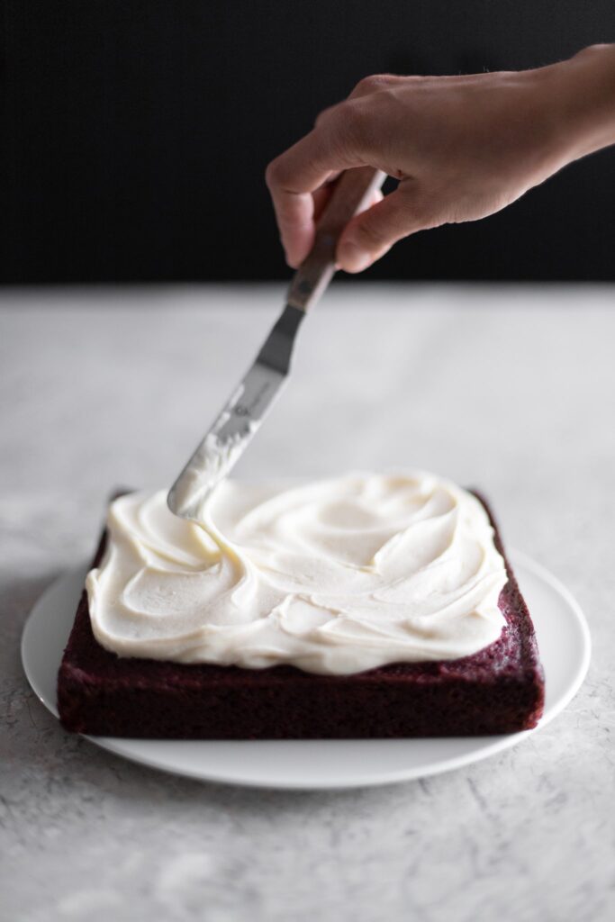 red velvet brownies being iced, photographed from a 45 degree angle