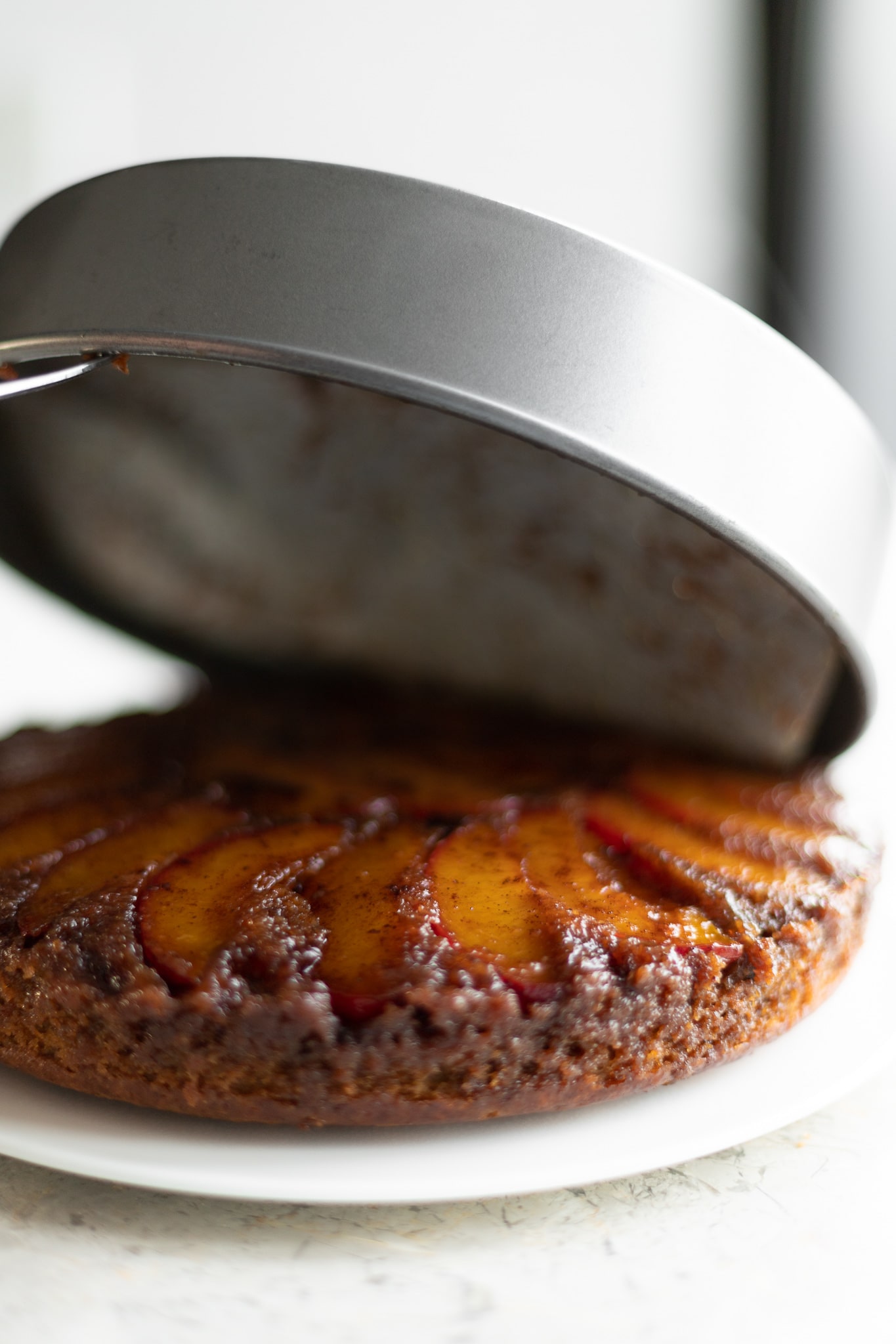 plum upside down cake, flipped over and the pan being removed to reveal the cake underneath