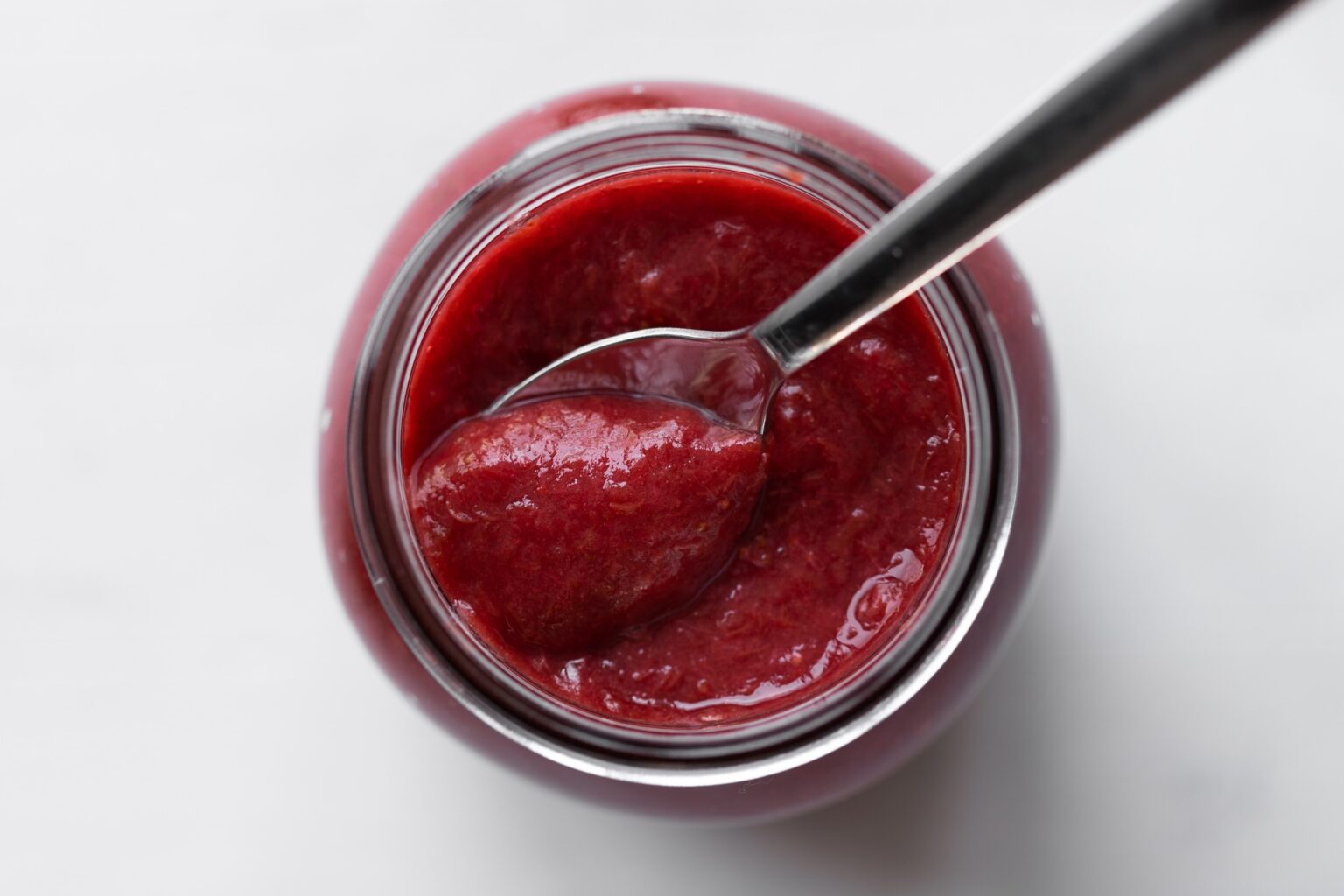 strawberry rhubarb compote in a jar with a spoon photographed from overhead